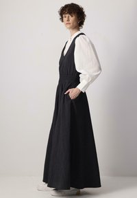 Mustmustel linen kleit sügava V-kaelusega, smockitud vöökohaga ja külje taskutega. Omab pikka, voolavat siluetti, koos valge pluusi ja sneakers'itega.