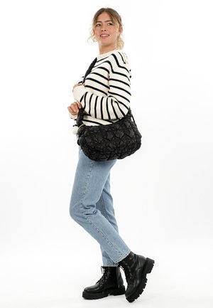 Black quilted shoulder bag with a rounded, textured design and a wide strap, paired with a striped sweater and blue jeans.