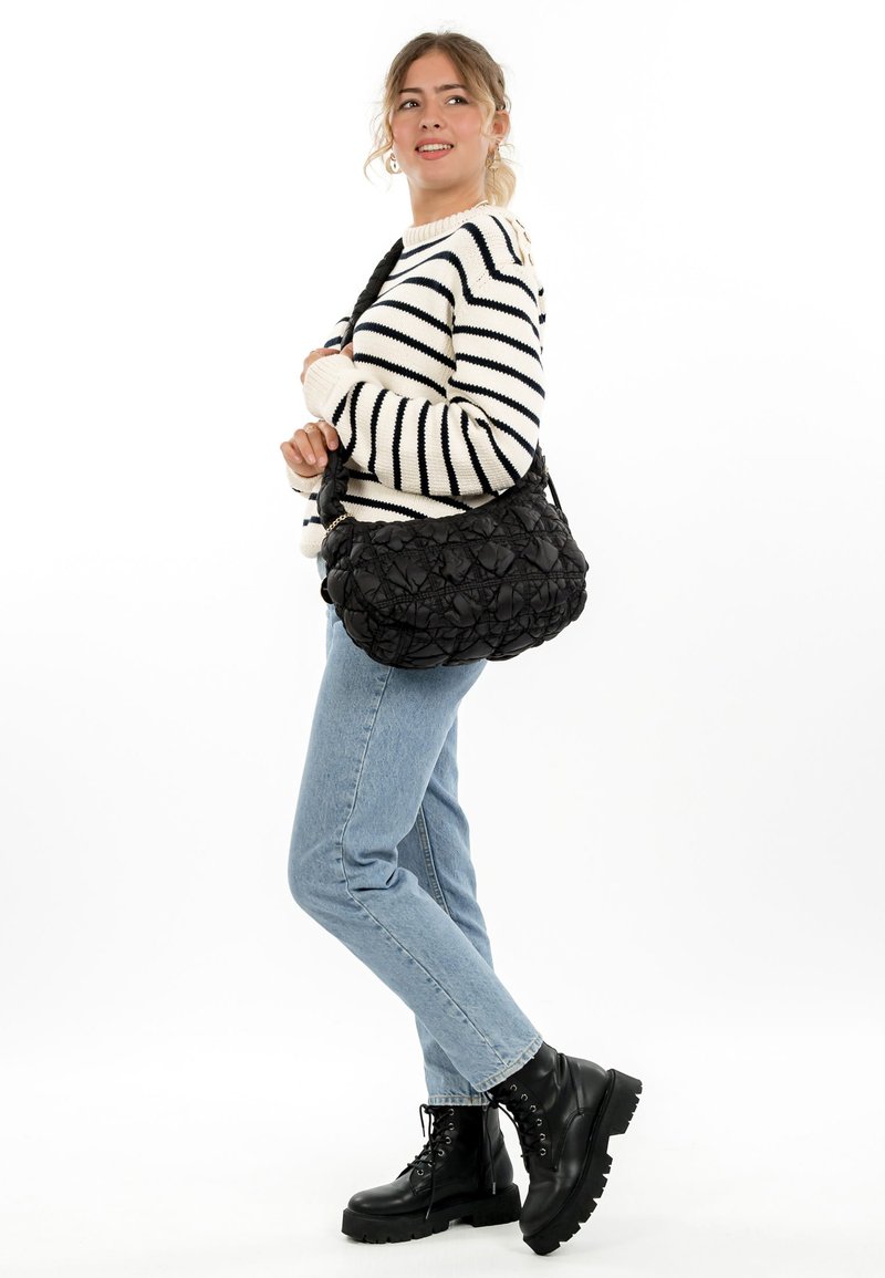 Black quilted shoulder bag with a rounded, textured design and a wide strap, paired with a striped sweater and blue jeans.