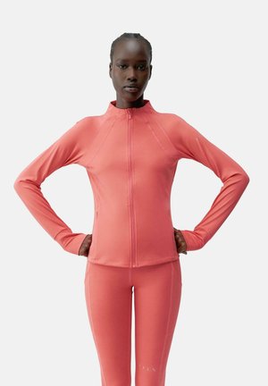 Chaqueta atlética ajustada en coral brillante, hecha de una tela suave y elástica. Presenta un cuello alto, mangas largas y una cremallera frontal completa.