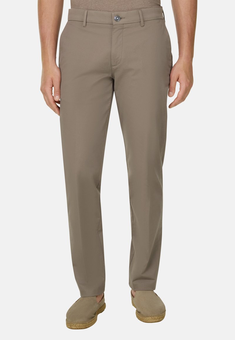 Homme portant un pantalon beige à coupe droite et des chaussures plates assorties, debout devant un fond clair uni.