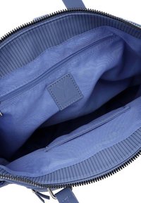 Blue interior of a bag featuring a zippered pocket, smooth fabric texture, and a logo patch. Top has a ribbed trim and zipper closure.