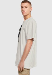 Tricou din bumbac gri deschis, cu mâneci scurte, gât rotund și imprimeu grafic negru pe față. Croială dreaptă, textură minimă, design casual.