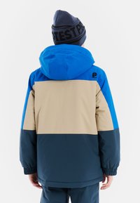 Niebieska, beżowa i ciemnozielona wodoodporna kurtka z kapturem. Posiada elastyczne mankiety oraz logo na górnej części pleców. Gładka tekstura.