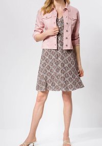 Růžová džínová bunda se stříbrnými knoflíky přes hněd dress s vzorem. Šaty mají rozšířený lem a kulatý výstřih.