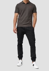 Polo shirt gris foncé avec un col et des manches courtes, associé à un pantalon de jogging noir. Des baskets blanches avec des accents noirs complètent le look.