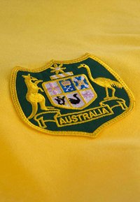 Geborduurde groene en gouden schildvormige badge met een kangaroe, een emoe en decoratieve elementen met "AUSTRALIË" aan de onderkant.