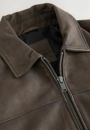 Brown leather jacket featuring a collared neckline and front zipper closure. Textured surface with visible stitching and branding tag inside.