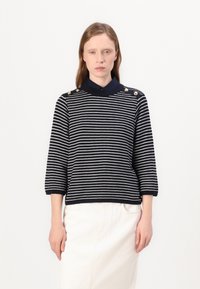 Pulover cu dungi albastre și albe, cu mâneci până la trei sferturi, având un guler și accente de butoane aurii pe umăr.