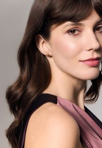 Złote kolczyki o skręconym wzorze, z gładkimi powierzchniami, noszone przez modelkę z średniej długości brązowymi włosami, na neutralnym tle.