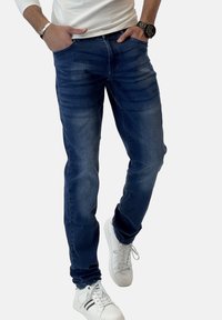 Jeans oscuros de corte ajustado, con detalles desgastados y una textura suave, combinados con zapatillas blancas.
