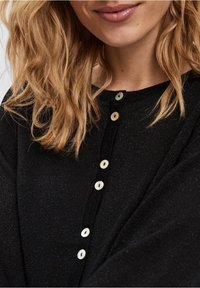 Cardigan nera con scollo rotondo, caratterizzata da bottoni iridescenti lungo la parte anteriore. Il tessuto ha un leggero luccichio e una consistenza morbida.