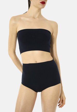 Donna che indossa un crop top nero senza spalline e biancheria intima nera a vita alta su uno sfondo chiaro e uniforme.