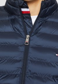 Navy puffer jacket with a high collar, horizontal quilted design, full zipper, and contrasting red and white striped accents inside the collar.