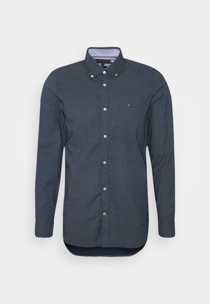 Mørkeblå skjorte med lange ærmer, knapper foran, hvidt mikropunktsmønster, knappet krave og lille logo på venstre bryst.