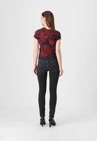 Blusa corta de manga corta con estampado rojo, combinada con vaqueros oscuros y tacones negros. La blusa presenta diseños en espiral y una silueta ajustada.