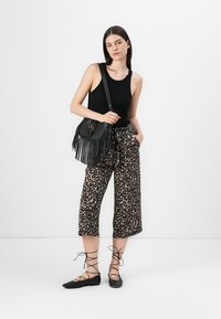 Débardeur noir, pantalon court à imprimé léopard, sac à main à franges noir, ballerines lacées noires. Texture lisse et design décontracté dans l'ensemble.