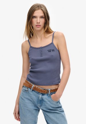 Różowa, żebrowana bluzka na ramiączkach z koronkowym wykończeniem i detalami w postaci guzików, w połączeniu z jasnoniebieskimi, luźnymi dżinsami i plecionym brązowym paskiem.