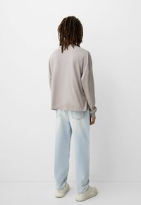 Lys grå langærmet skjorte med dropped shoulders, parret med lys blå loose-fit jeans og beige sneakers. Minimalistisk design uden mønstre.