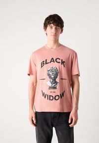 Růžové bavlněné tričko s černým grafickým potiskem bystu, který obsahuje text "BLACK WIDOW" a "EST 1993", krátké rukávy a kulatý výstřih.