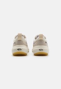 Beige og hvite basketballsko har en overdel i semsket skinn og tekstil, rund form, trekkflik ved hælen, og en strukturert gummisåle.