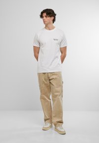 Hvid bomulds T-shirt med sort tekst, parret med beige cargo bukser og creme sneakers. Simpelt design, korte ærmer, afslappet pasform.