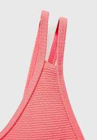 Koralen roza športni modrček z teksturirano rebrasto tkanino. Ima tanke naramnice in brezšivne robove za udobje. Na splošno lahka zasnova.