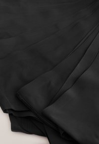 Črna tkanina z mehko teksturo, ki ima večplastno pršenje in gladko, tekočo zasnovo. Robovi so čisto zaključeni brez vidnih šivov.