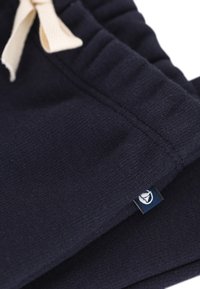 Marineblaue Jogginghosen mit weicher Textur, ausgestattet mit einem elastischen Bund und einem cremefarbenen Kordelzug. Mit einem kleinen Markenschild.