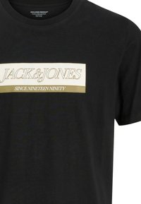 Schwarzes Baumwoll-T-Shirt mit einem weißen rechteckigen Grafik, die den Text "JACK&JONES" und "SINCE NINETEEN NINETY" in goldenen Buchstaben zeigt.