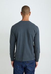Langermet grå t-skjorte laget av myk stoff, med rund hals og en tettsittende design, kombinert med blå denimjeans.