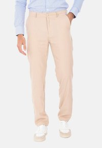 Pantaloni beige in una vestibilità slim, con tasche laterali, chiusura a bottone e tessuto morbido, abbinati a sneaker bianche.