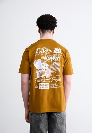 Bruine katoenen t-shirt met grote witte grafische tekst en illustraties op de achterkant, waaronder schoenen en sportartikelen, met korte mouwen.