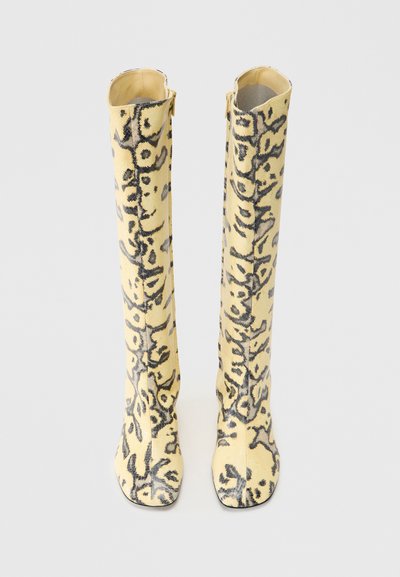 Κίτρινες μπότες μέχρι το γόνατο με μαύρο λουλουδάτο σχέδιο, κατασκευασμένες από μαλακό ύφασμα. Σχεδιασμός με τετράγωνη μύτη και φερμουάρ στο πλάι για εύκολη φορεσιά.
