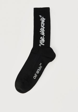 Calcetín corto negro con parte superior acanalada, logo "Off-White" blanco en el pie y texto "See Nothing" en blanco en la zona de la pantorrilla.