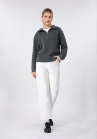 Γκρι ριμπ πλεκτό πουλόβερ με μισό φερμουάρ και κουκούλα, συνδυασμένο με λευκά παντελόνια φαρδιάς γραμμής και μαύρα αθλητικά παπούτσια. Απλός, καθημερινός σχεδιασμός ένδυσης.