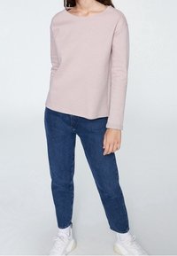 Haut rose clair à manches longues avec un col arrondi, associé à un jean tapered bleu foncé et des baskets blanches. Texture lisse, design décontracté.