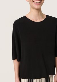 Black, short-sleeve top with a round neckline, made of smooth fabric. Features a loose fit and a clean hemline, paired with a striped skirt.