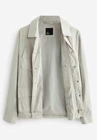 Chaqueta gris claro hecha de tejido texturizado. Presenta un cuello con solapa, bolsillos frontales y cierre de botones a presión con cremallera.