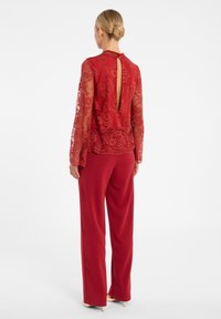 Rode kanten top met een hoge hals en een sleutelgatachterkant, gecombineerd met rode broek met wijde pijpen. Lange doorzichtige mouwen en een gegolfde zoom. 