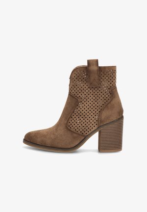 Bota de tobillo de ante marrón con tacón grueso apilado y detalles de panel lateral perforado sobre fondo blanco.