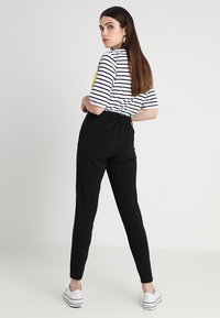 Calças pretas ajustadas com uma cintura elástica, combinadas com uma blusa de meia-manga às riscas com um gráfico. Modelo de costas, usando ténis.