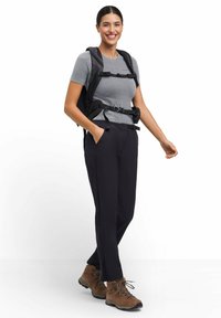 Strój na zewnątrz, składający się z szarej koszulki z krótkim rękawem, czarnych spodni trekkingowych i brązowych butów do wędrówek. Czarny plecak z regulowanymi paskami.