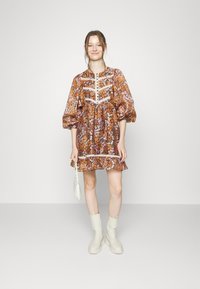 Vestido com padrão floral em tons de laranja e roxo, com mangas bufantes, acabamento branco e saia rodada. Par de botins de camurça creme e uma pequena bolsa.