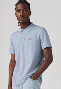 Light blue cotton polo shirt with a two-button placket and short sleeves. Features a small red Levi's logo on the left chest.
