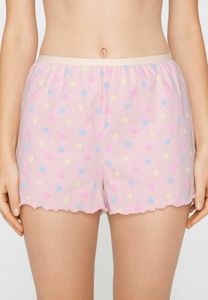 Rosa weiche Stoffshorts mit kleinen blauen, gelben und rosa Herzmustern, die an der Taille getragen werden, sichtbar vom Bauch bis zu den oberen Oberschenkeln.