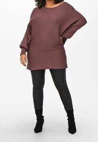 Överdimensionerad bordeauxröd ribbad tröja med vid halsringning och långa, lösa ärmar, ihop med smala svarta skinnliknande byxor och svarta ankelstövlar.