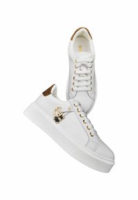 Witte sneakers van soepel leer met een gestructureerde bruine accent op de hiel, gouden hardware en een platte rubberen zool. Heeft een vetersluiting.