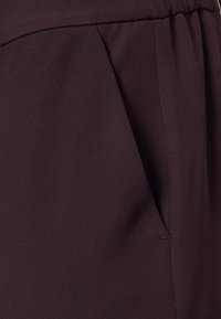 Donkerbruin, gestructureerde stof met een zijzak en geplooide details. Glad oppervlak met een gestructureerde uitstraling, geschikt voor formele kleding.