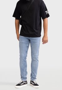 Camiseta de algodón negra, corte holgado, con logotipo blanco en la manga. Jeans ajustados de mezclilla azul claro. Zapatillas negras con acentos y cordones blancos.